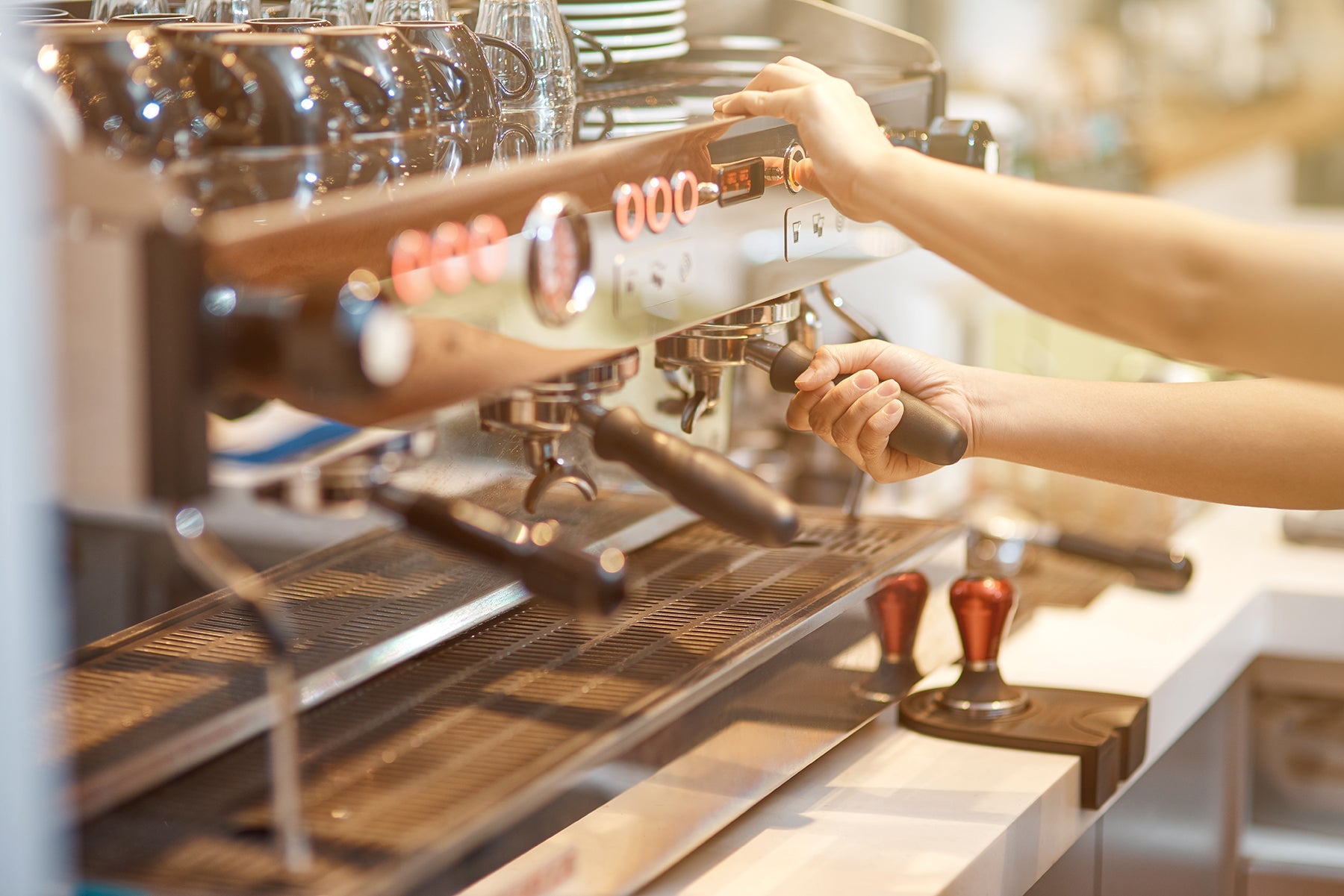 Photo of a barista placing a portafilter basket into a shiny chrome espresso machine.